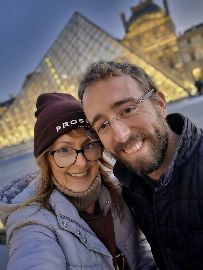 Selfie d’Ania et Luke devant la pyramide du Louvre illuminée, le soir