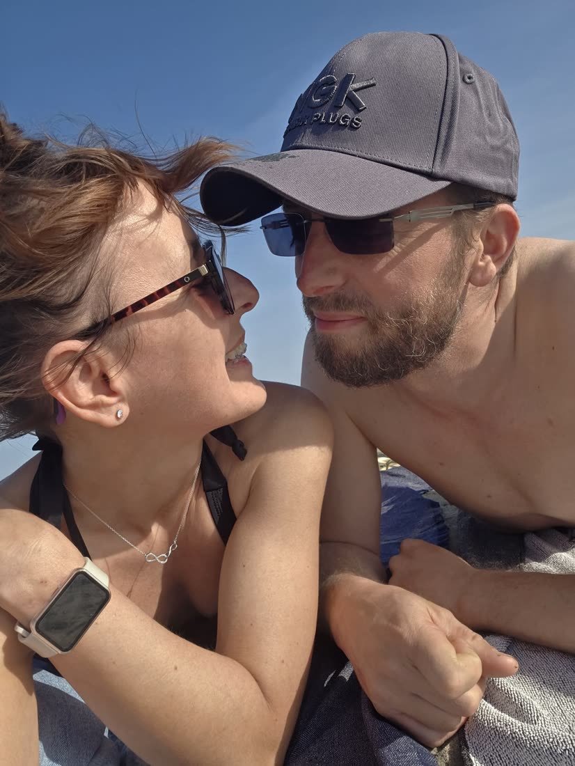 Ania et Luke allongés sur une serviette de plage, sous le soleil, se regardent en souriant