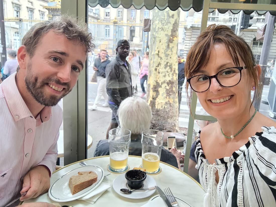 Ania et Luke attablés à une terrasse de café parisienne, deux bières sur la table